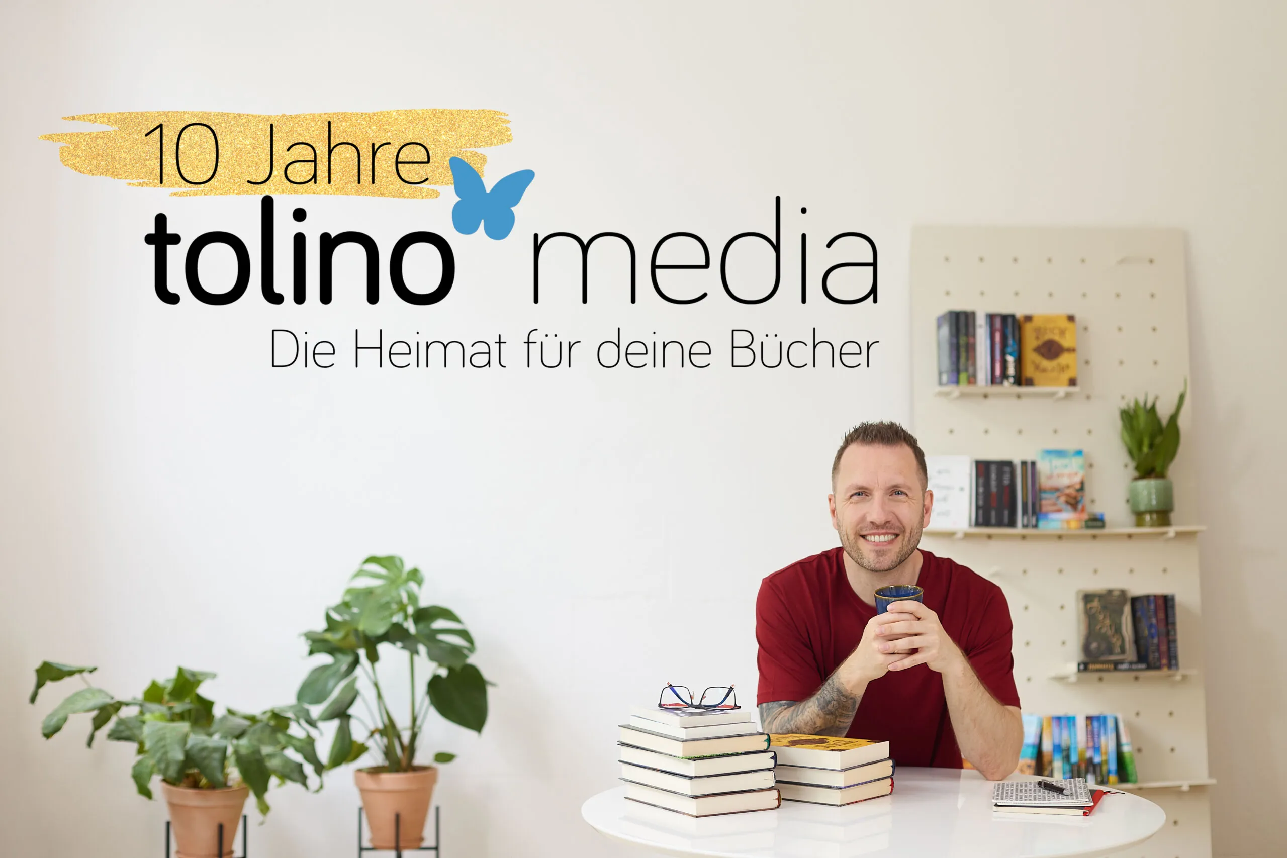 Titelbild zur Pressemitteilung zum 10-jährigen Jubiläum von tolino media. Zu sehen ist ein Mann an einem Tisch. Er lächelt in die Kamera, vor ihm liegen zwei Stapel Bücher. Im Hintergrund ist ein Bücherregal zu sehen. In der linken Bildhälfte steht das Logo von tolino media: 10 Jahre tolino media Die Heimat für deine Bücher".